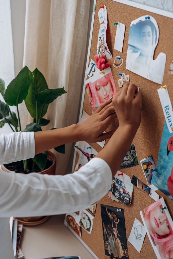 A person arranging photos and notes on a cork board, adding a personal touch to a creative workspace.