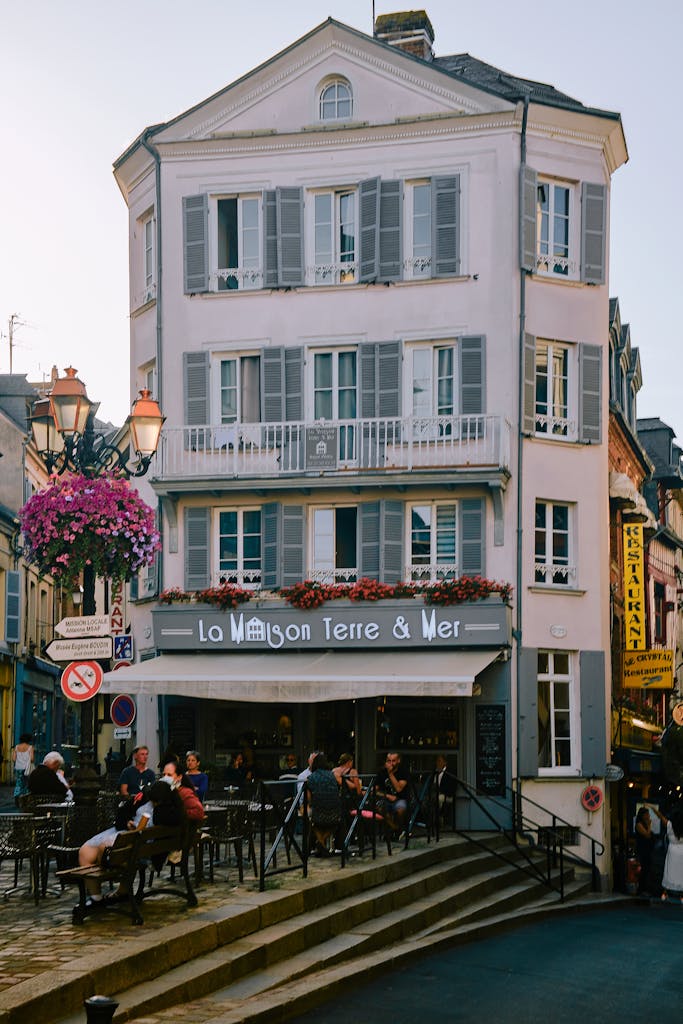 Street view of a classic Honfleur cafe with people enjoying outdoor dining under street lamps.