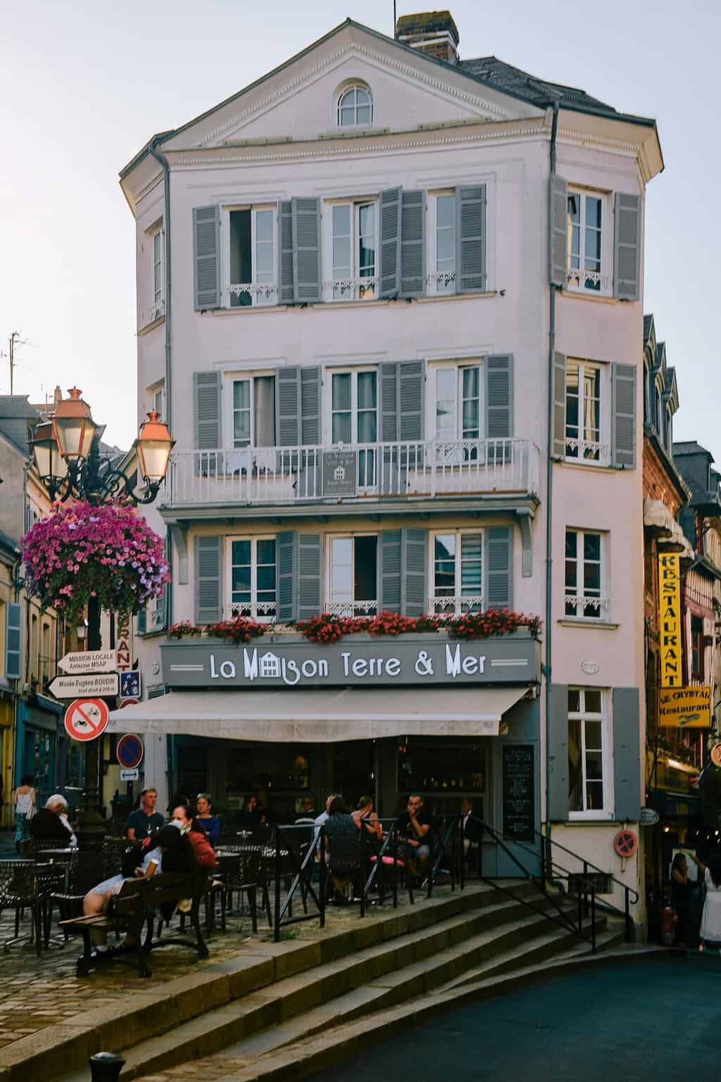 Street view of a classic Honfleur cafe with people enjoying outdoor dining under street lamps.