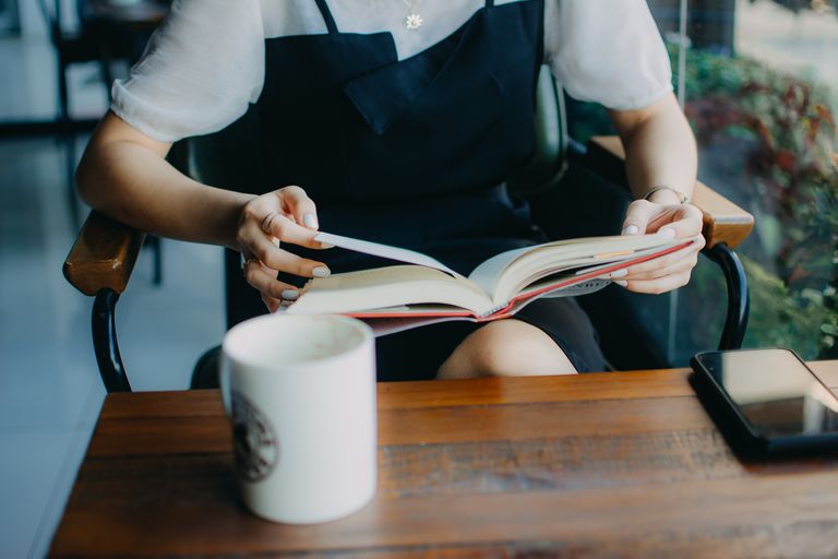 A woman reading a book with coffee in a cozy cafe environment.