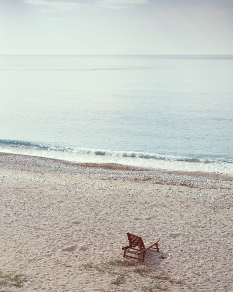 Peaceful beach scene with a lone wooden chair by the gentle waves, perfect for relaxation.