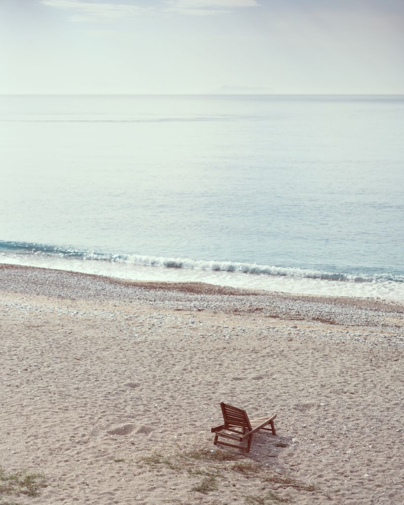 Peaceful beach scene with a lone wooden chair by the gentle waves, perfect for relaxation.