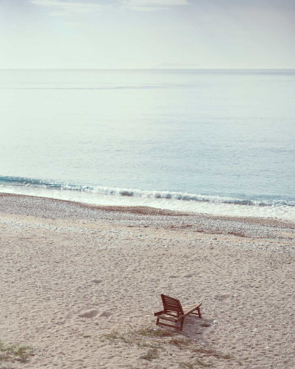 Peaceful beach scene with a lone wooden chair by the gentle waves, perfect for relaxation.